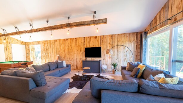 A modern living room with wooden panel walls, a pool table, and a large window providing a view of the outdoors. - Lush Chalet Near Lake of Butgenbach (Buellingen)