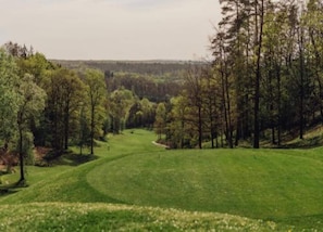 Een golfbaan met een verzorgd fairway, omgeven door dichte bomen en een heuvelachtig landschap.