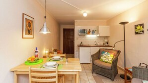 Une cuisine compacte équipée d’un four à micro-ondes, d’un évier et de meubles blancs. Un coin repas avec une table et des chaises en bois est situé à côté de la cuisine.
