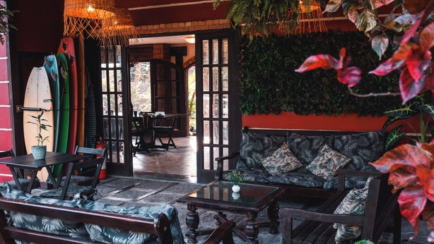 A cozy lounge area with a sofa and chairs, a table, and a surfboard rack. - Bacana Hotel Boutique (Búzios)