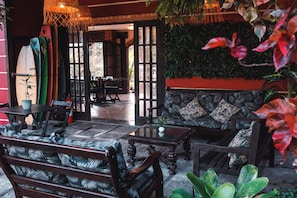 A cozy lounge area with a sofa and chairs, a table, and a surfboard rack. - Bacana Hotel Boutique (Búzios)