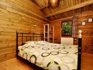A wooden cabin bedroom with a bed, a window, and a radiator.