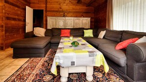 En hyggelig stue med en hjørnesofa, et mønstret tæppe og et træloft.