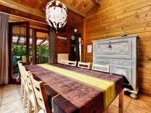 A wooden dining room with a table set for four, a chandelier, and a view of greenery outside.