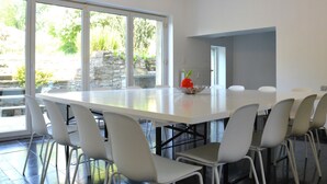 A modern dining area with a large white table and white chairs, large windows with a view of greenery, and pendant lighting. - Family Retreat, Forested Anhee (Anhée)