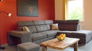 A modern living room with a grey sectional sofa, a wooden coffee table with fruit, and a red accent wall. - Elegant Child Friendly Villa in Berismenil near Forest (La Roche-en-Ardenne)