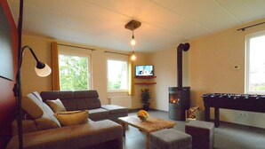 A living room with a sofa, ottomans, a coffee table, a fireplace, a television, and a foosball table. - Elegant Child Friendly Villa in Berismenil near Forest (La Roche-en-Ardenne)