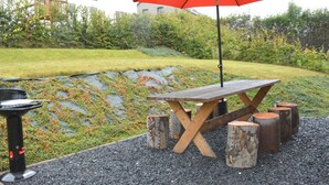 A wooden picnic table with a red umbrella, surrounded by wooden stools and a black grill. - Elegant Child Friendly Villa in Berismenil near Forest (La Roche-en-Ardenne)