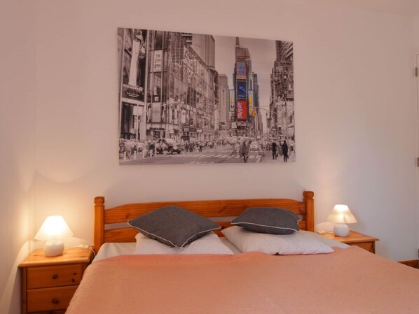 Une chambre à coucher avec un lit, deux tables de chevet et un tableau accroché au mur représentant une rue animée.