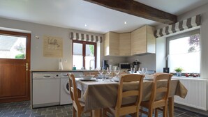 A kitchen with a dining table set for four, wooden chairs, a washing machine, and a window with a view of the outside. - Cottage Near Spa F1 Circuit (Stavelot)