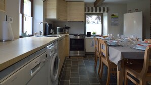 A modern kitchen with a washing machine, microwave, and oven. There is a dining area with a table set for four. - Cottage Near Spa F1 Circuit (Stavelot)