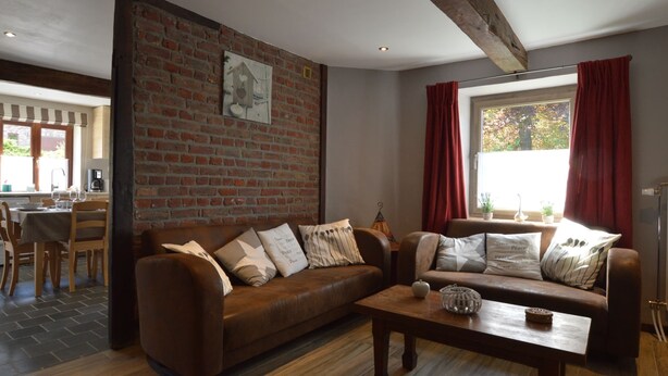 A cozy living room with a brown leather sofa, a wooden coffee table, and a brick wall with a picture. - Cottage Near Spa F1 Circuit (Stavelot)
