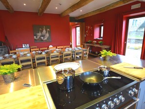 A kitchen with a stove, pots, and a dining area with chairs and a table. - Holiday Home in Falaen With Garden BBQ (Mettet)