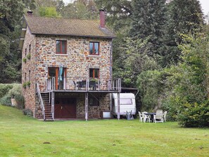 A stone house with a balcony, a white van, and outdoor furniture.