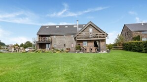Uma casa de dois andares com varanda, um pátio com mobiliário de exterior e um gramado bem cuidado.