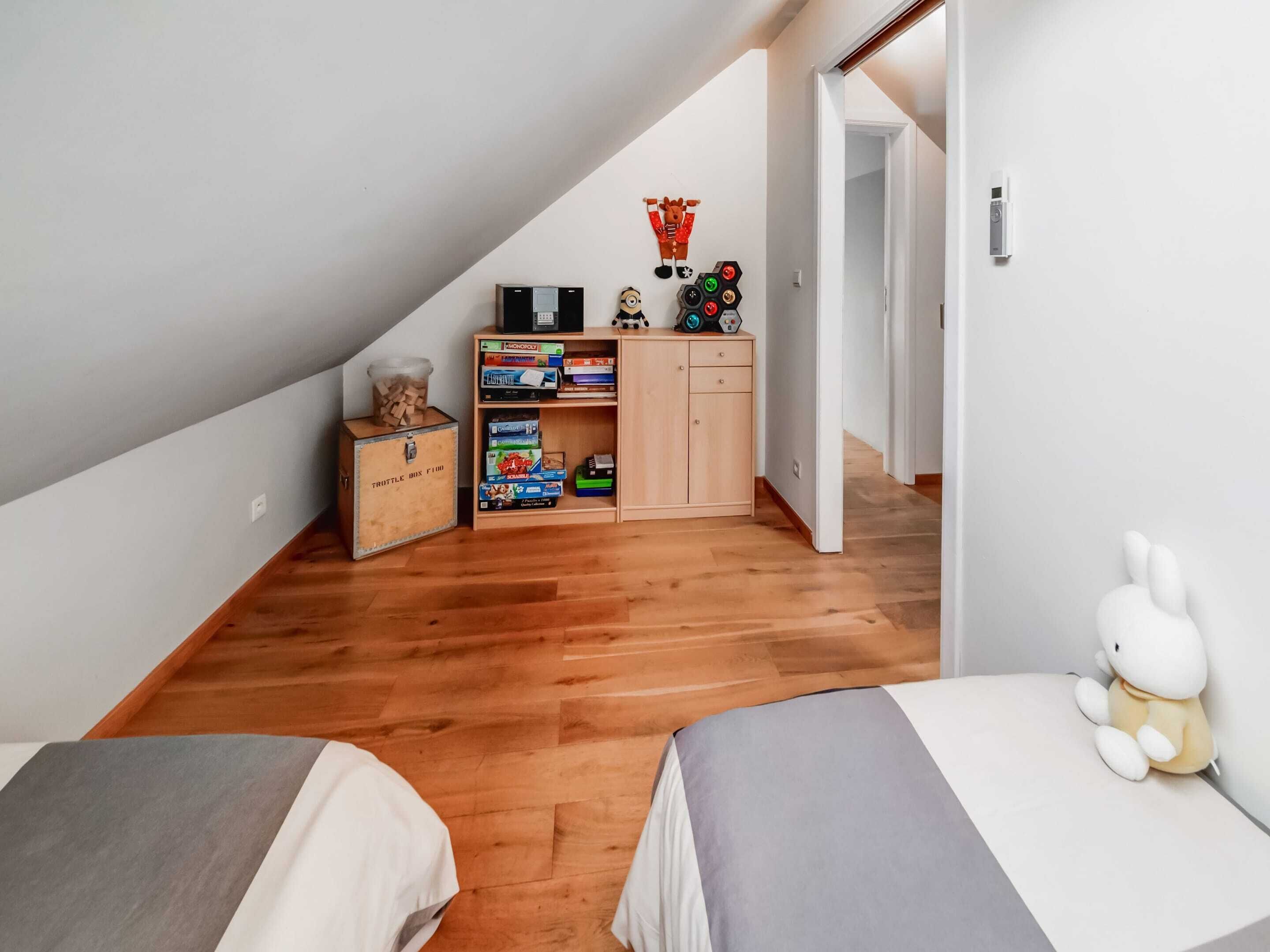 Een knus zolderkamer met houten vloeren, een hoogslaper, een klein bureau en een boekenplank vol met gezelschapsspellen.