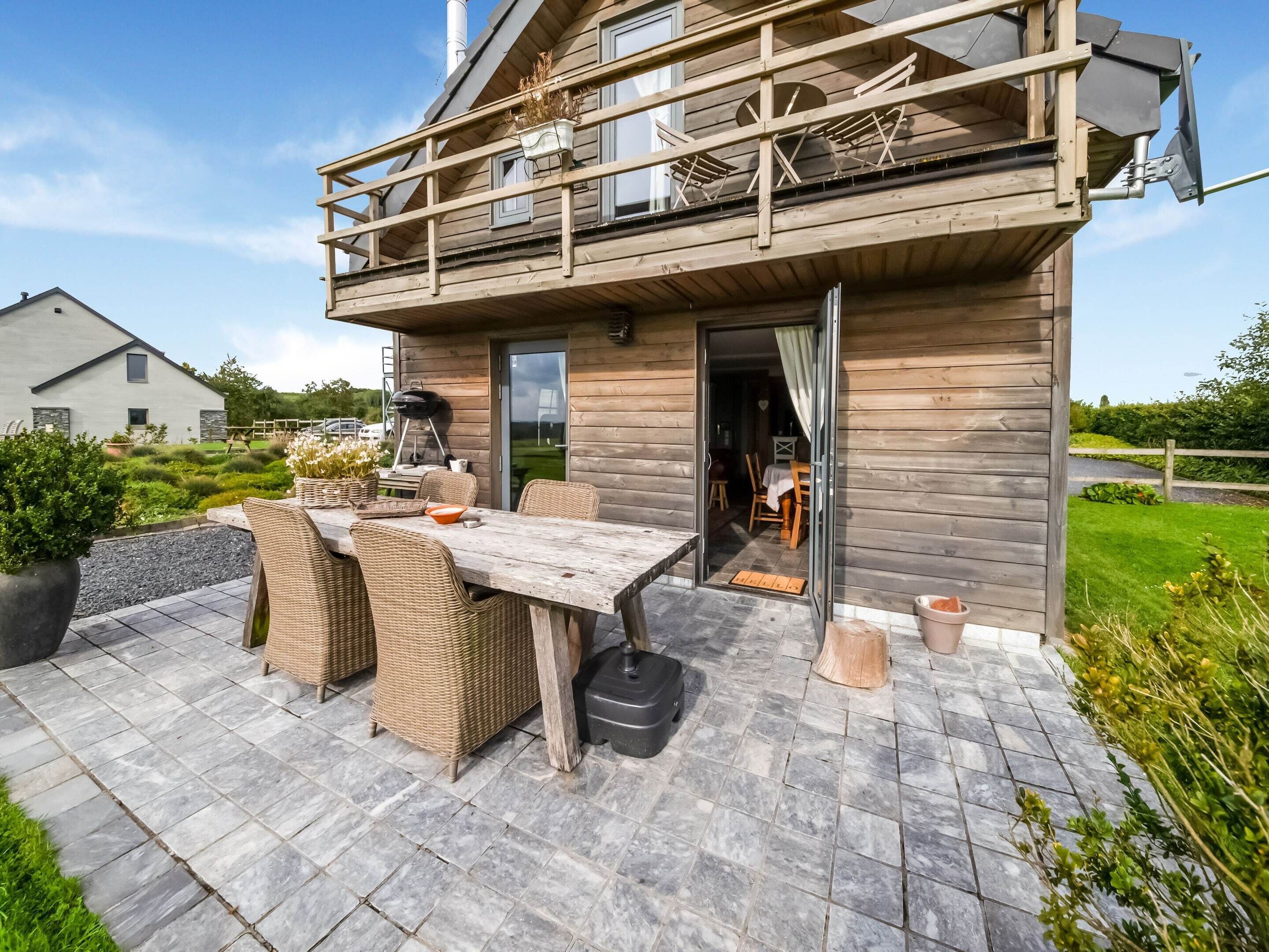 A wooden cabin with a balcony, outdoor dining area, and a view of the surrounding landscape.