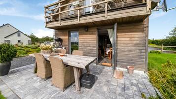 A wooden cabin with a balcony, outdoor dining area, and a view of the surrounding landscape.