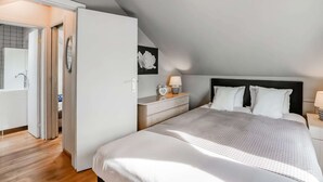 Quarto com cama grande, mesa de cabeceira, luminária na parede e porta para um banheiro.