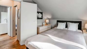 Quarto com cama grande, mesa de cabeceira, luminária na parede e porta para um banheiro.