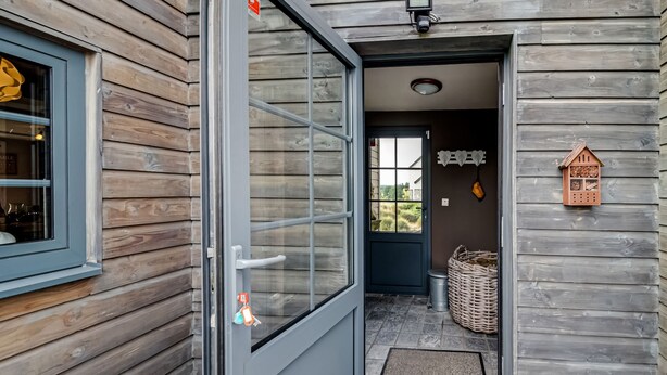 Fachada de madeira com porta de vidro que dá para uma área de entrada com piso ladrilhado.