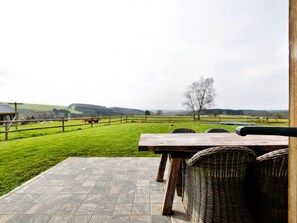 A patio with a table and chairs overlooking a grassy field with a fence and a tree. - Petit Wilogne Holiday Home in Mont (Houffalize)