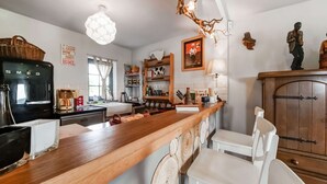 Uma cozinha com bancada de madeira, cadeiras brancas, cafeteira e um armário.
