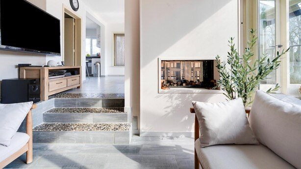 Een moderne woonkamer met een flatscreen televisie, een houten dressoir, een bank en een raam met uitzicht op een tuin.