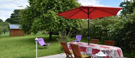 An outdoor patio with a table set for four, surrounded by chairs, a red umbrella, and a white lantern.