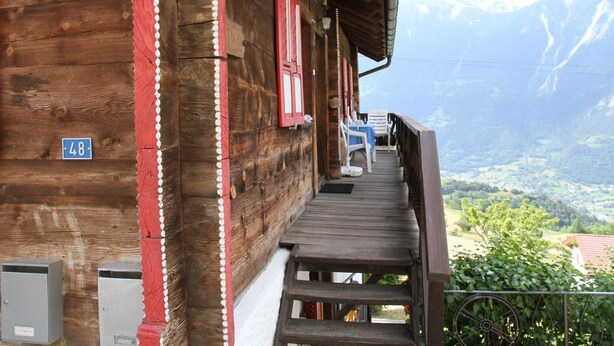 A wooden building with a balcony, a blue sign with the number 48, and a view of a mountainous landscape. - Boutique Apartment in Valais With Balcony (Guttet-Feschel)