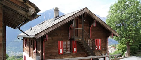 A wooden chalet with a steep roof, red shutters, and a wooden staircase leading to the entrance.