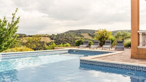 Une piscine entourée de chaises longues, de verdure et de collines.