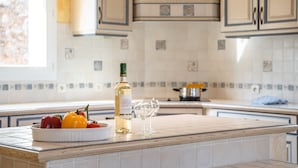 Une cuisine avec un mur recouvert de carreaux, une bouteille de vin et un saladier de fruits.