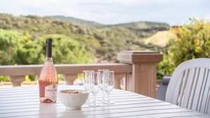 Une table avec une bouteille, des verres et un bol, placée sur une terrasse offrant une vue panoramique.
