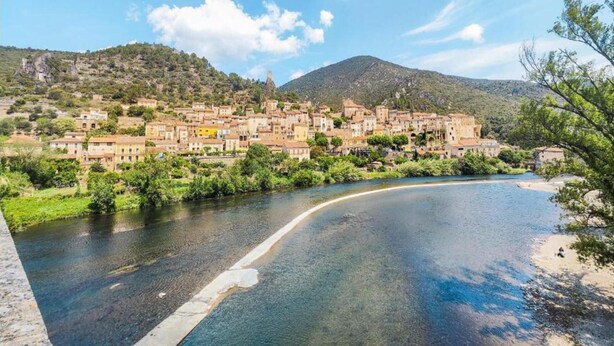 Une ville côtière avec des bâtiments le long d’une rivière, une plage et une montagne en arrière-plan.
