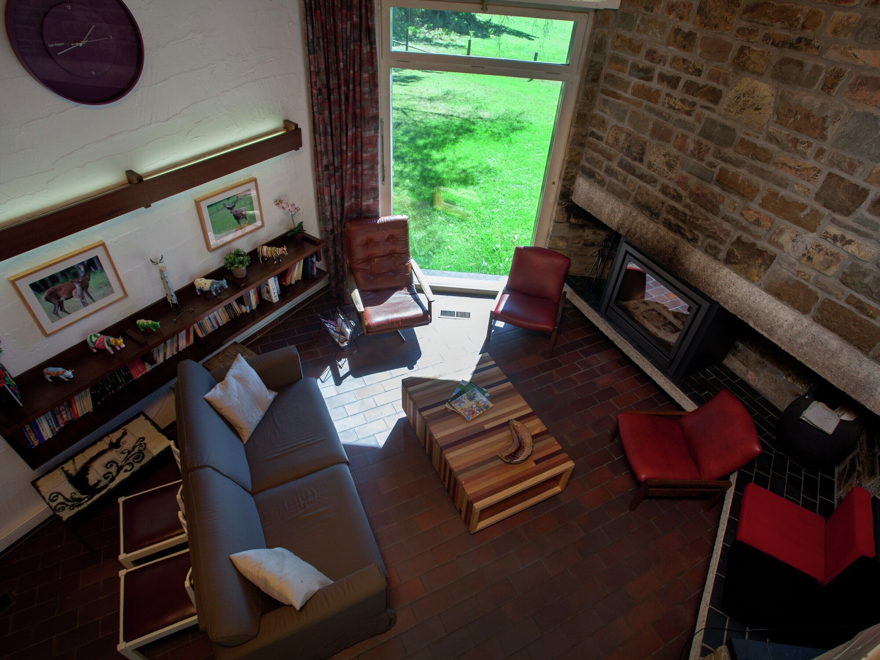 A cozy living room with a fireplace, a sofa, a red armchair, and a bookshelf filled with books and decorative items.