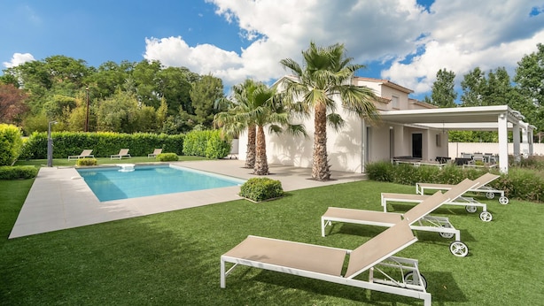 Ein Pool mit Liegestühlen, Palmen und einem Gebäude mit überdachter Terrasse.