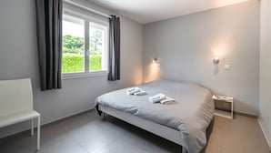 Ein modernes Schlafzimmer mit einem Bett, einem weißen Stuhl, einem Nachttisch und einem Fenster mit Vorhängen.