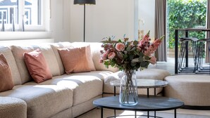 A modern living room with a beige sectional sofa, a glass vase with flowers on a round table, and a floor lamp. - Charming Villa With Indoor Swimming Pool, Near the Beach and Town Centre (Koksijde)