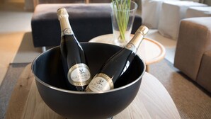 A bowl containing two bottles of champagne with labels, placed on a wooden table in a living room with a sofa and a vase of flowers in the background. - Charming Villa With Indoor Swimming Pool, Near the Beach and Town Centre (Koksijde)