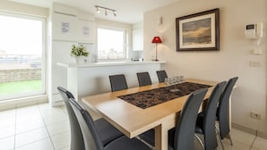 A modern kitchen with white cabinets, a large window, and a dining area with a wooden table and chairs. - Penthouse With 2 Terraces and Sea/casino Views (Middelkerke)