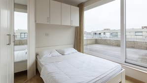 A modern bedroom with a large window, a bed, and built-in wardrobe. - Penthouse With 2 Terraces and Sea/casino Views (Middelkerke)