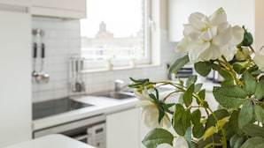 A modern kitchen with white cabinets, a window, and a plant with white flowers. - Penthouse With 2 Terraces and Sea/casino Views (Middelkerke)