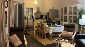 Ein großzügiger Wohnbereich mit hoher Decke, freiliegenden Holzbalken, einem Esstisch mit Stühlen, einer Küche im Hintergrund und einer gemütlichen Sitzecke mit Sofa und Sesseln.