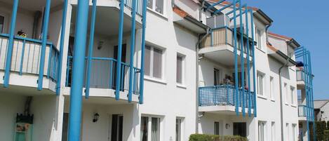A multi-story residential building with balconies, a flat roof, and a well-maintained lawn.