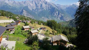 A mountainous village with traditional wooden houses, a stone wall, and a clear view of the surrounding peaks.