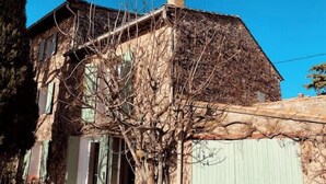 Un bâtiment rustique en pierre, avec un grand arbre devant, un portail en métal et un petit jardin.