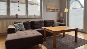 Una sala de estar moderna con un sofá modular, una mesa de centro de madera y ventanas grandes con persianas.