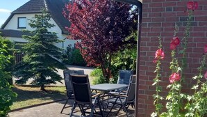 Un patio al aire libre con una mesa y sillas, un muro de ladrillo y un jardín con flores y un árbol.