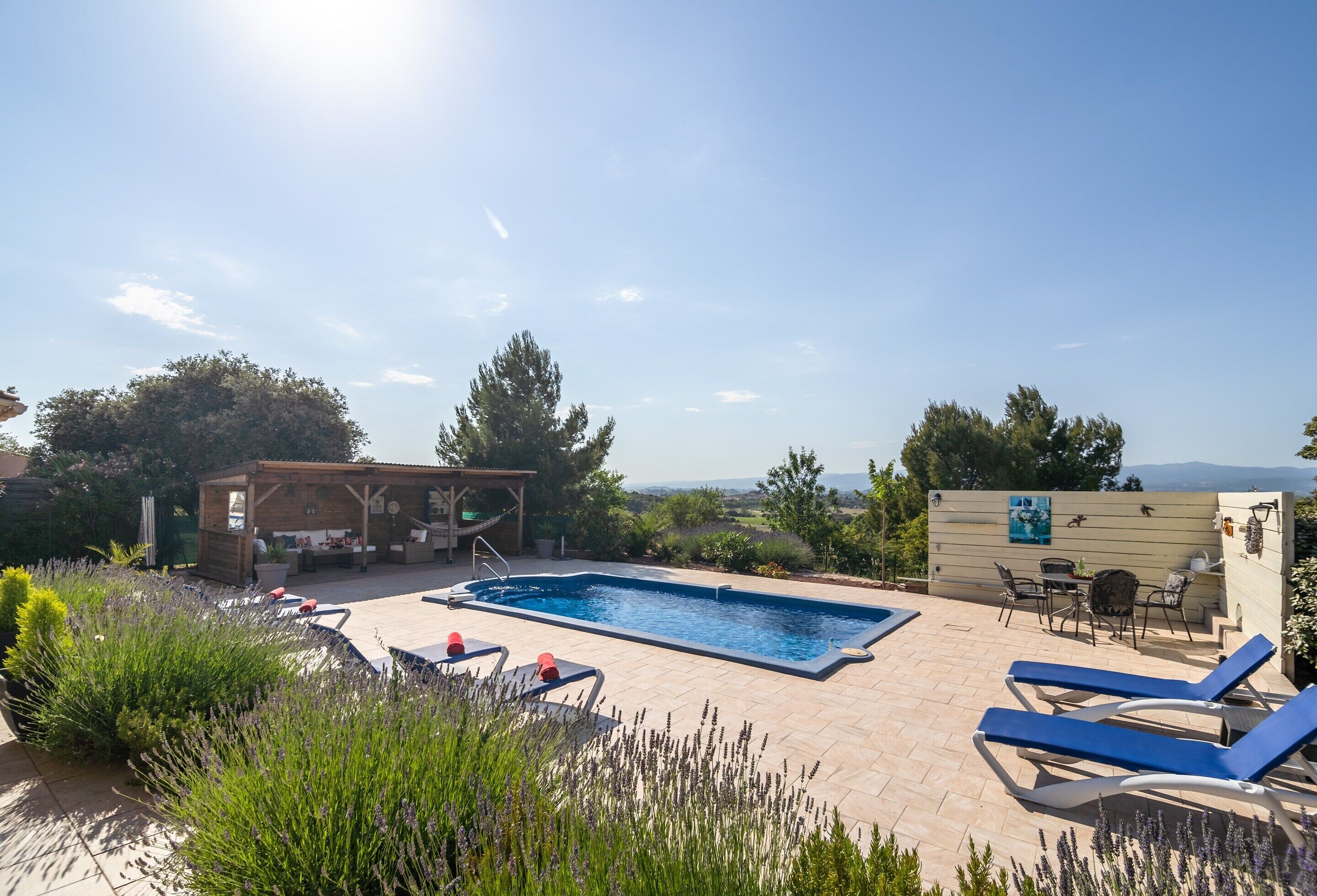 A swimming pool with lounge chairs, a wooden pergola, and a view of the landscape.